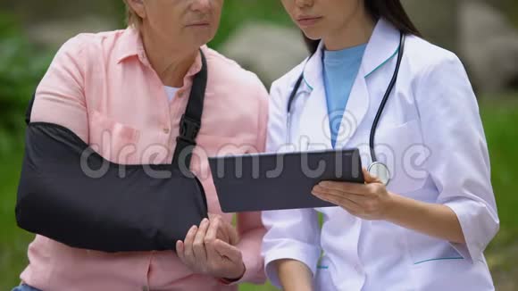 女治疗师给受伤的老太太展示手臂吊带平板电脑图像康复中心视频的预览图