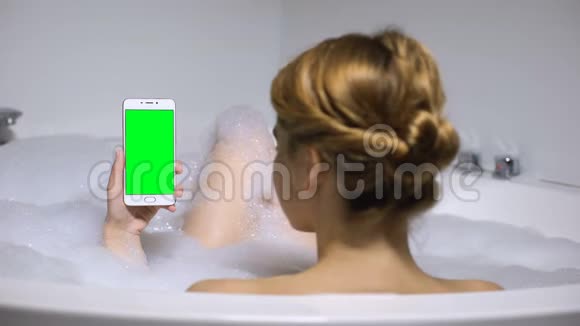 沐浴的女人拿着绿色屏幕的智能手机聊天社交网络视频的预览图