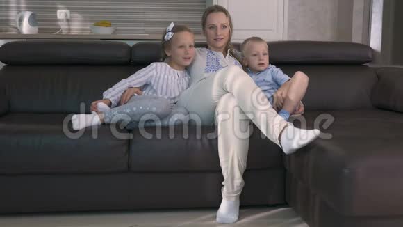 妈妈和两个孩子坐在沙发上看电视视频的预览图
