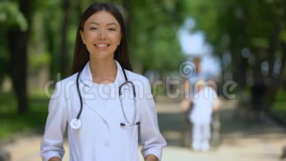 微笑女医生在康复中心附近的公园里看镜头视频的预览图
