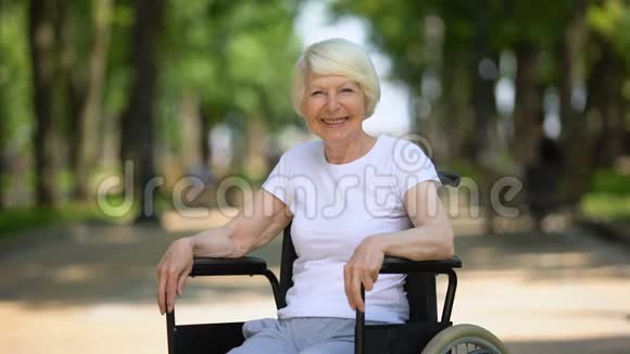 轮椅上的老年妇女微笑着看着镜头公园里阳光明媚视频的预览图