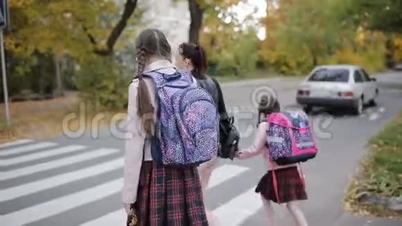 母亲带着女儿在秋天放学回家在十字路口过马路视频的预览图
