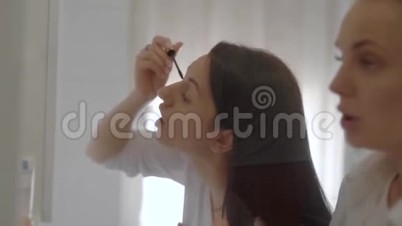 室内拍摄的两名年轻女子站在镜子前的早晨和化妆视频的预览图