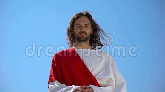 耶稣身穿长袍在蓝天的背景下祈祷请求上帝宽恕罪人视频的预览图