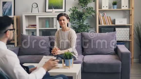 开朗的女人和坐在办公室沙发上的心理咨询师交谈视频的预览图