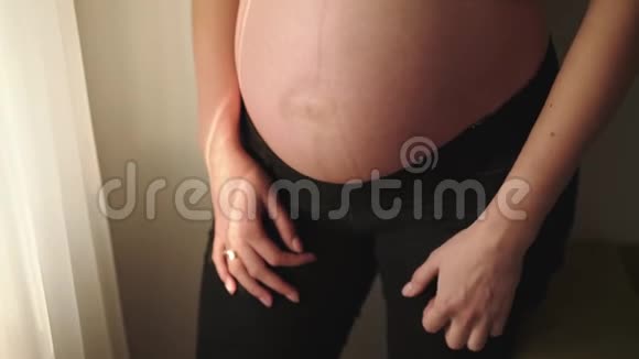 无法辨认的孕妇在房间的窗户上抚摸着她的腹部视频的预览图