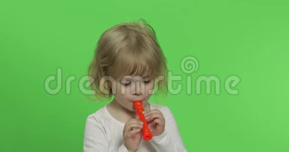 三岁金发女孩在绿色背景下玩具烟斗上玩耍的肖像视频的预览图