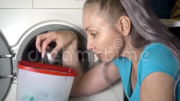 年轻女子准备在洗衣机里洗衣服拿出并打开装有洗衣粉的盒子视频的预览图
