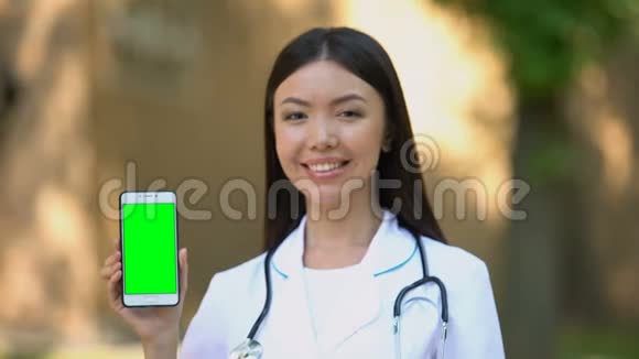 微笑的女医生展示智能手机相机上有绿色屏幕健康视频的预览图