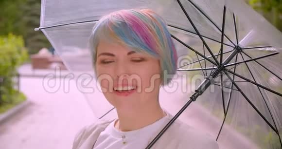 年轻可爱的白种人女性的特写镜头染着头发撑着伞看着镜头开心地笑着视频的预览图