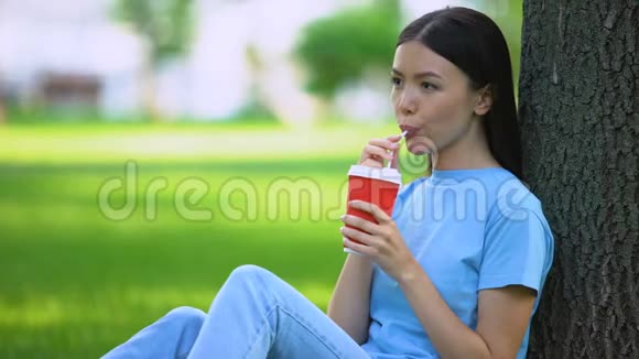 快乐的雌性通过稻草坐在花园树上喝柠檬水提神视频的预览图