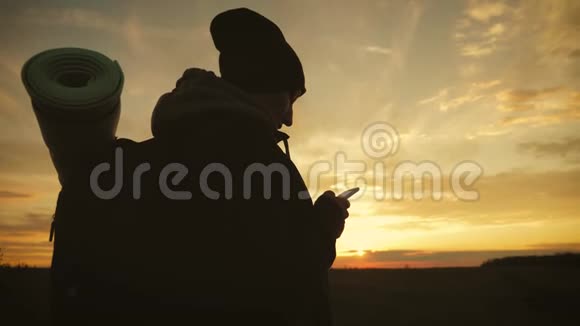 年轻旅游女性的剪影使用电话与戏剧性的日落天空背景一直联系在一起视频的预览图