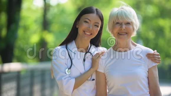 护士抱着幸福的老年妇女微笑着进入镜头一天在医院公园视频的预览图