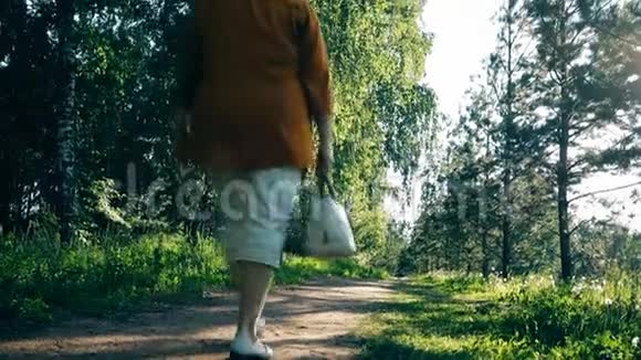 一位老年妇女在阳光明媚的一天走在森林小径上视频的预览图