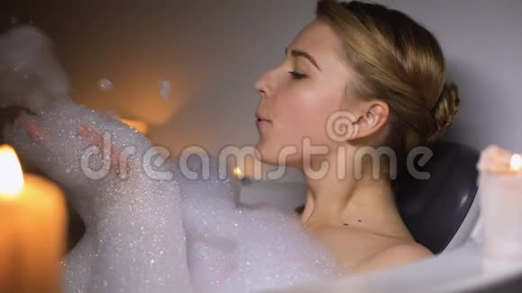 可爱的女人在浴室吹泡泡玩得开心晚上用蜡烛放松视频的预览图