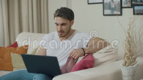 快乐的男人在家里的沙发上用笔记本电脑庆祝成功视频的预览图