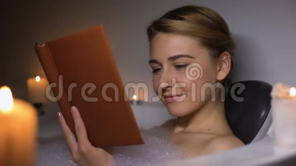 年轻女子在浴缸里用泡沫和蜡烛看书晚上放松视频的预览图