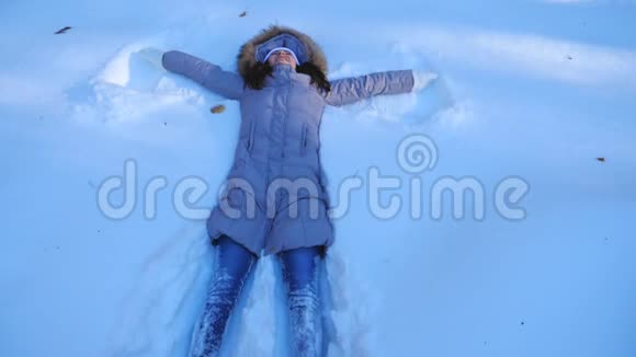 年轻的女孩躺在雪地草地上做天使快乐的女人在雪地里玩享受冬天的时光快乐的女士视频的预览图