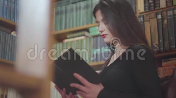 深色头发的女孩在书架背景下图书馆看书的肖像视频的预览图