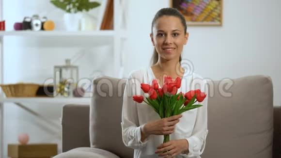 美丽的年轻女子一束郁金香坐在沙发上对着镜头微笑视频的预览图