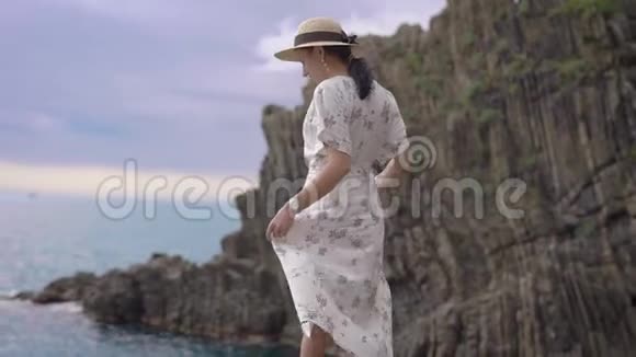 迷人的年轻黑发戴着帽子穿着轻盈的夏装站在悬崖边看着相机视频的预览图