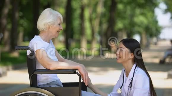 公园的微笑护士与残疾老年妇女交谈康复中心视频的预览图