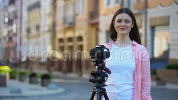 女操作员站在城市街道上的三脚架摄像机旁视频的预览图
