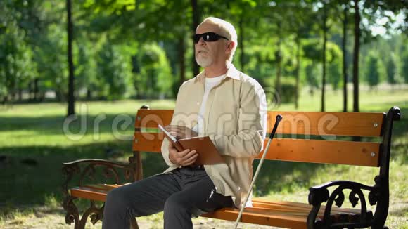 盲人看盲文书坐在夏季公园的长椅上休息视频的预览图