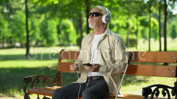 盲人老人把耳机电缆放在电话里听语音信息录音簿视频的预览图