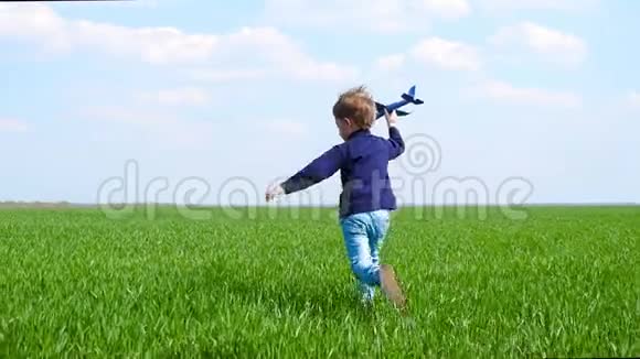 一个快乐的孩子手里拿着一架玩具飞机慢悠悠地沿着绿色草坪奔跑视频的预览图