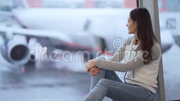 年轻女子坐在靠近窗户的机场背景模糊的飞机视频的预览图