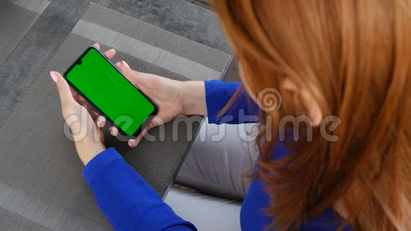 红发女孩坐在咖啡馆里使用带有绿色屏幕的手机快关门视频的预览图