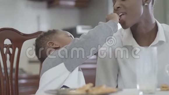 非裔美国妇女和她的小儿子坐在桌子旁一起玩饼干家庭健康早餐视频的预览图