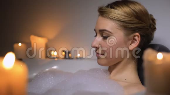 晚上年轻女性在泡沫泡沫和蜡烛的温暖浴中放松视频的预览图