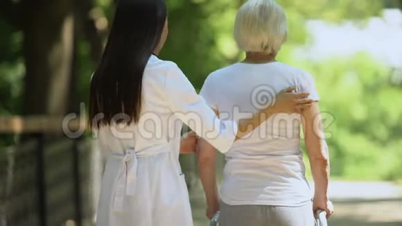 女治疗师帮助老年妇女在公园里移动步行架康复视频的预览图