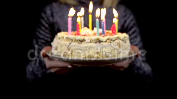 一个女孩拿着蜡烛对着镜头拿出一个节日蛋糕孤立的黑色背景视频的预览图