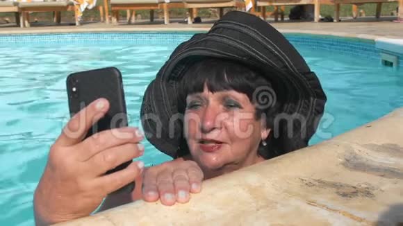 一位戴着黑帽子的白人老年女性正在视频通话正在一个蓝色的游泳池里游泳视频的预览图