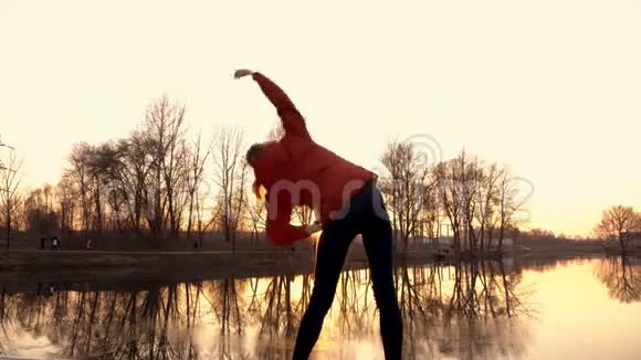 日落时在城市公园里做运动的小女孩她在河岸上做体操和伸展运动视频的预览图