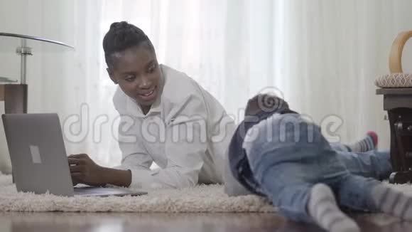 在地毯上工作的非裔美国妇女和她可爱的小儿子来到她面前要求她注意视频的预览图