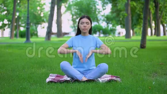 迷人的年轻女士坐在公园里坐着莲花姿势在户外放松视频的预览图