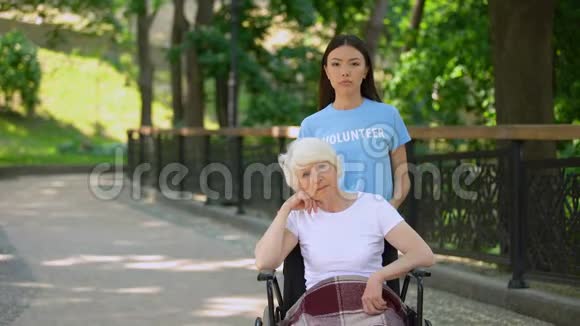 坐在轮椅上的老太太和悲伤的志愿者在户外看相机临终关怀视频的预览图