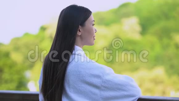 酒店阳台上站着享受自然景观的酒店浴袍快乐女人视频的预览图