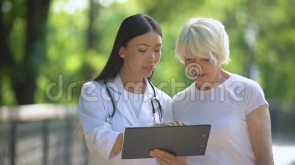 微笑护士显示医院公园内老年妇女检查结果视频的预览图