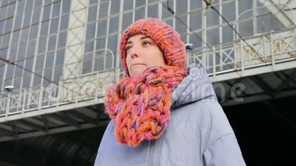 在阳光明媚的寒冷日子里一位穿着蓝色外套戴着五颜六色帽子的年轻女子在火车站特写冬天的肖像视频的预览图