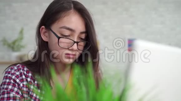 漂亮的亚洲女孩戴着长头发的眼镜在家里的客厅里带着笔记本电脑学习或搜索视频的预览图
