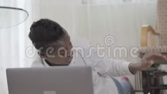 非裔美国妇女在地毯上的笔记本电脑上工作她可爱的小儿子朝她扔了一个玩具视频的预览图