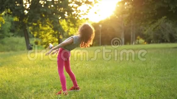 穿裙子的快乐小女孩跳在公园草地上做杂技轮夏季户外活动动作缓慢视频的预览图