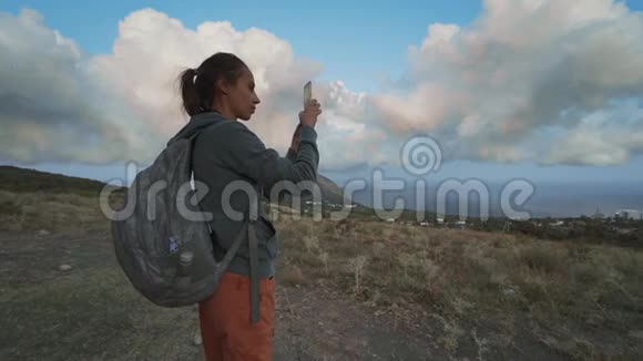 女徒步旅行者看着美丽的多云的日落天空用手机拍照视频的预览图