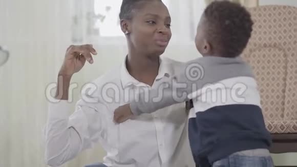 快乐自信美丽的非裔美国女人在舒适的客厅里逗她可爱的小儿子笑视频的预览图