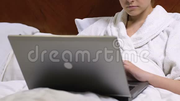 女士自由职业者穿着浴袍手提电脑坐在酒店床上出差视频的预览图